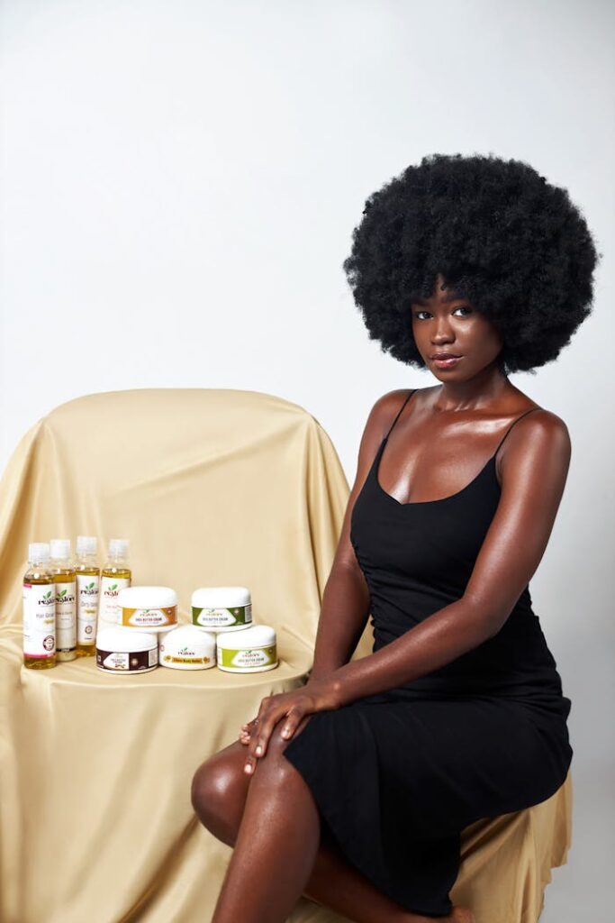 Studio portrait of an African American woman in a black dress with beauty products on a table.