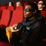 A person watching a 3D movie while eating popcorn in a cinema.